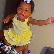 Kalani is registered to the contest to win money with this photo: baby, child, smiling, yellow_dress, white_bow, indoor, person, happy, cute, portrait, skin, hand, footwear, adult_hand, sandal, fashion, infant, joyful, holding, celebration