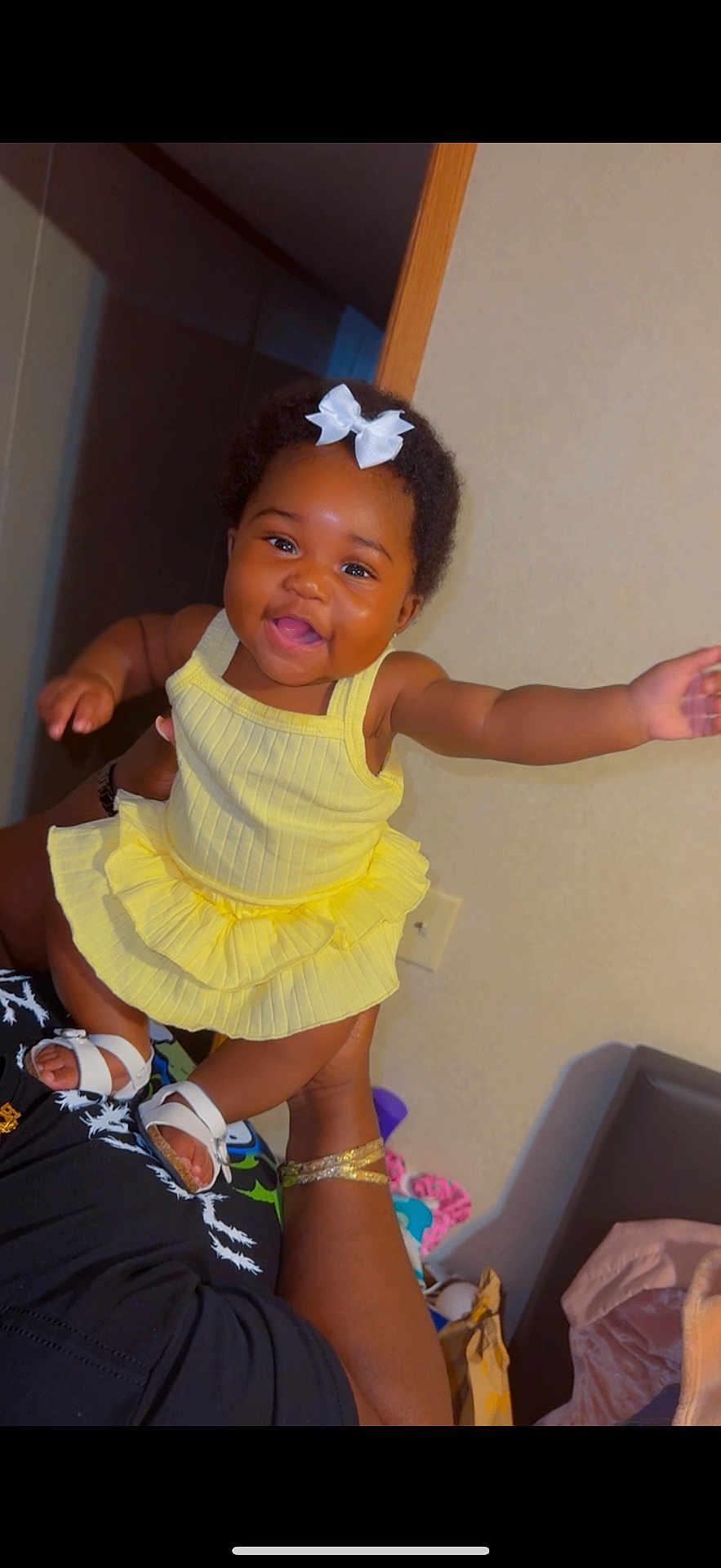 Kalani is registered to the contest to win money with this photo: baby, child, smiling, yellow_dress, white_bow, indoor, person, happy, cute, portrait, skin, hand, footwear, adult_hand, sandal, fashion, infant, joyful, holding, celebration