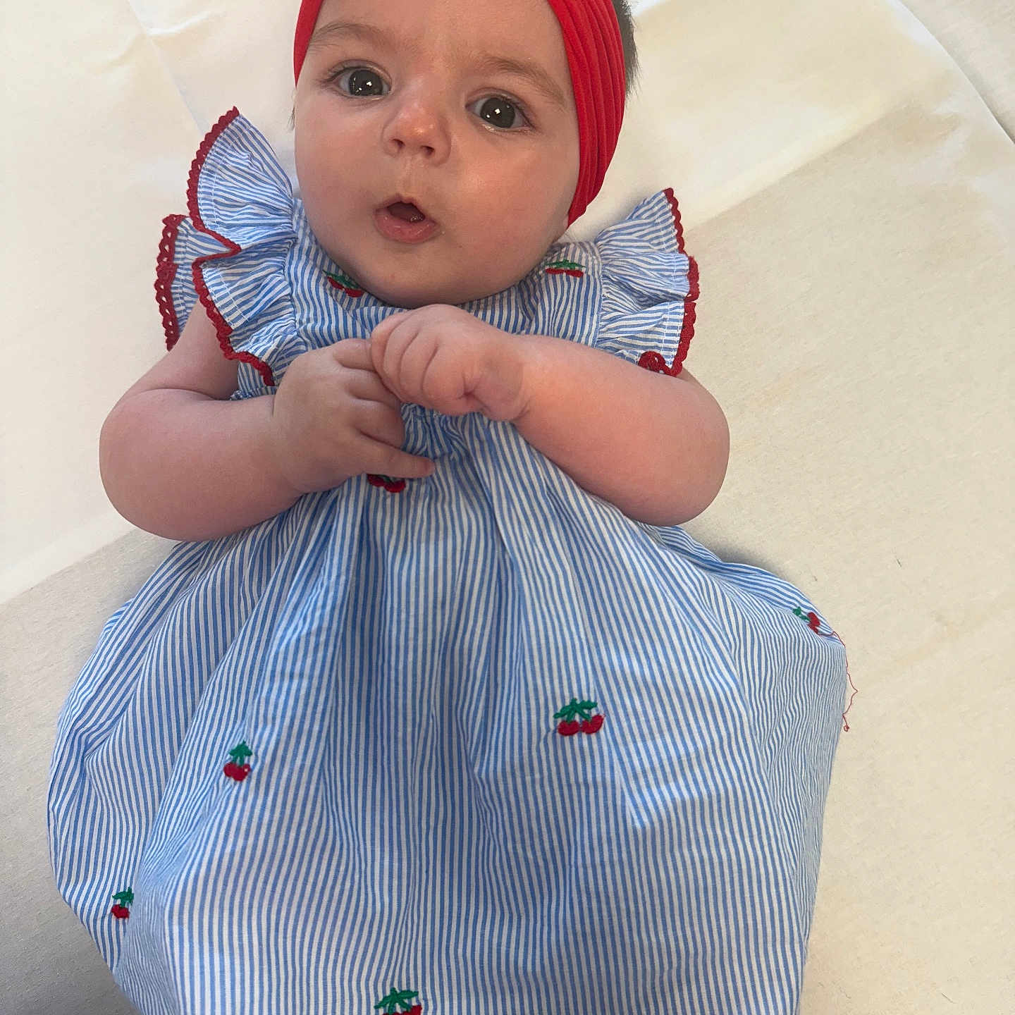Rae joined the competition — help win amazing prizes! adorable, baby, blue, cherry_pattern, child, closeup, clothing, cute, expression, eyes, face, hands, headband, infant, lying_down, portrait, red, skin, striped_dress, white_background