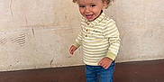 Ali a rejoint le concours — aidez-le/la à gagner de superbes lots ! toddler, child, curly_hair, striped_shirt, polo_shirt, blue_jeans, sneakers, standing, smiling, happy, indoor, wall, floor, person, young_child, casual_clothing, portrait, full_body, light_skin, cute