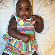 Eliana joined the competition — help win amazing prizes! baby, child, infant, colorful_clothing, headwrap, flower_accessory, striped_outfit, knitted_flowers, lying_down, white_quilt, cute, portrait, skin, hand, face, eyes, socks, bed, soft_lighting, indoors