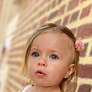 Laïss participe au concours pour gagner de l'argent avec cette photo : child, toddler, face, blue_eyes, hair_clip, curious, portrait, outdoor, brick_wall, skin, earring, expression, close_up, young_child, innocence, person, cute, head, looking, natural_light
