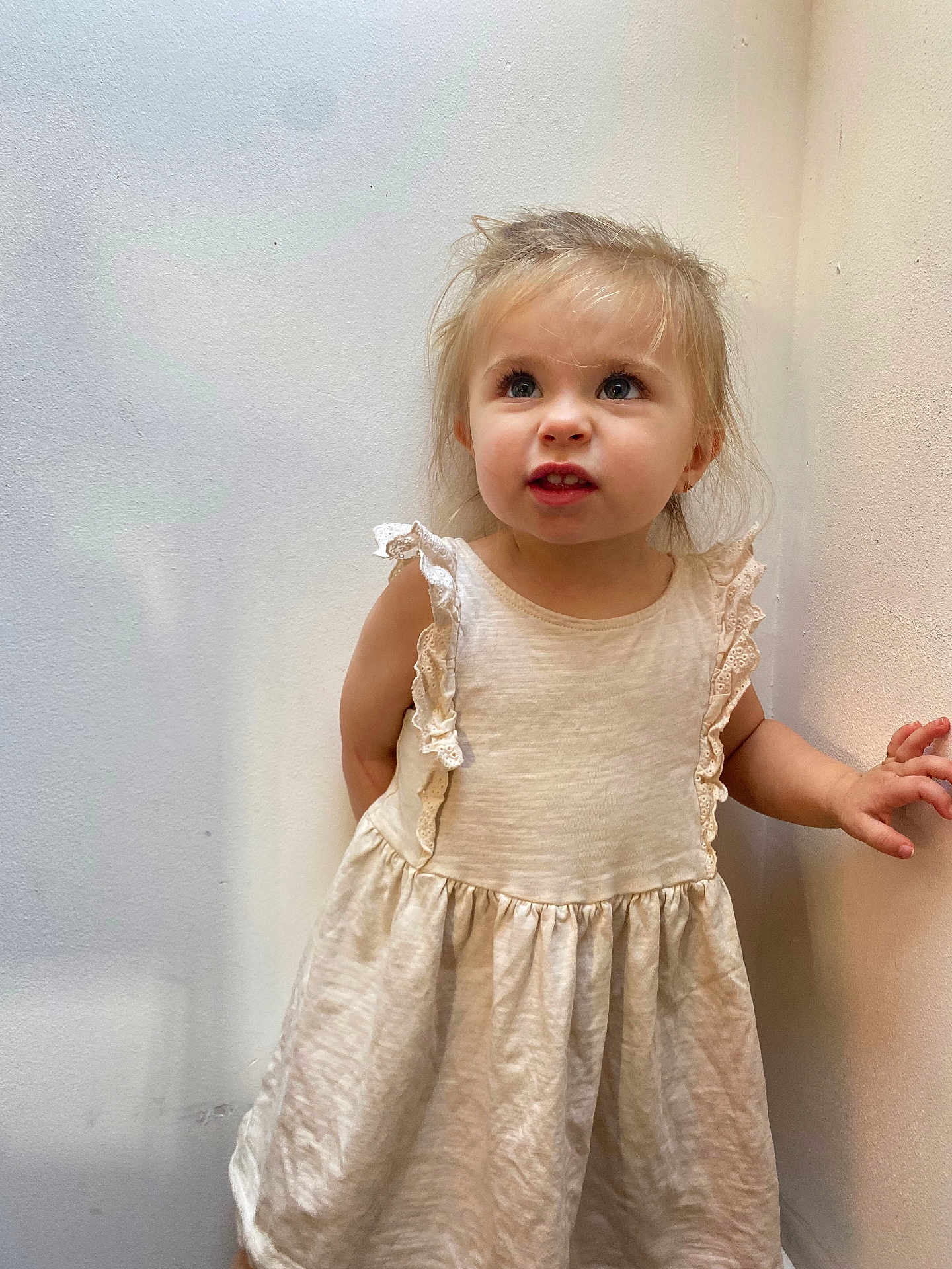 Laïss a rejoint le concours — aidez-le/la à gagner de superbes lots ! casual_clothing, child, cream_color, curly_hair, cute, dress, expression, girl, hands, indoor, innocent, light_skin, looking_up, person, portrait, small_child, standing, toddler, wall, young_child