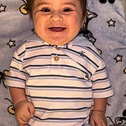 Ryan is registered to the contest to win money with this photo: baby, smiling, striped_clothing, polo_shirt, pants, blanket, cartoon_characters, lying_down, happy, child, infant, cute, face, cheerful, indoors, soft_texture, person, toddler, casual_clothing, playpen