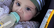 Ryan is registered to the contest to win money with this photo: baby, bottle, car_seat, blanket, hat, knitwear, infant, feeding, child, cute, portrait, closeup, indoors, clothing, face, person, safety, seatbelt, warning_label, resting