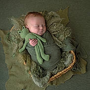 Evren is registered to the contest to win money with this photo: baby, sleeping, swaddled, plush_toy, frog, basket, blanket, green, cozy, infant, soft_texture, peaceful, cute, child, wrapped, portrait, indoors, resting, newborn, toddler
