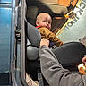 Daxtyn is registered to the contest to win money with this photo: baby, child, car, car_seat, seat, adult_arm, pouty_face, garage, workshop, rust, hand, clothing, vehicle_interior, curious, person, indoor, mechanic, repair, metal, blue_car