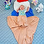 baby, infant, plush_toys, blanket, blue_blanket, quilted_blanket, mermaid_tail, cloth, fabric, cute, surprised_expression, soft_toys, stuffed_animals, colorful_toys, lying_down, indoors, child, young_baby, creative_photo, portrait