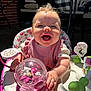 baby, child, smiling, happy, toy, pink, activity_center, sunlight, outdoor, face, person, clothing, seat, play, infant, table, cushion, hand, cute, expression