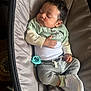 Jaylen is registered to the contest to win money with this photo: baby, sleeping, infant, clothing, pacifier, carrier, cushion, footwear, sneakers, grey_pants, green_shirt, white_onesie, hand, face, curly_hair, indoor, soft_lighting, peaceful, resting, child