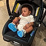 baby, infant, sleeping, car_seat, blue_sneakers, curly_hair, white_onesie, indoor, floor, footwear, child, person, seat, clothing, head, peaceful, rest, cute, small, toddler