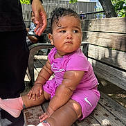 Willow is registered to the contest to win money with this photo: baby, bench, bracelet, child, curly_hair, expression, fence, hand, nature, outdoor, person, pink_clothing, seat, shade, skin, socks, sunlight, tree, water_droplets, wood