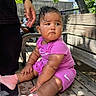 baby, bench, bracelet, child, curly_hair, expression, fence, hand, nature, outdoor, person, pink_clothing, seat, shade, skin, socks, sunlight, tree, water_droplets, wood