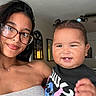 toddler, child, woman, glasses, smile, indoor, living_room, hair, pigtails, casual_clothing, portrait, family, happy, person, home, ceiling_fan, table, chair, decor, light