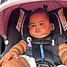 baby, car_seat, child, infant, pink_canopy, straps, outdoor, urban, sidewalk, black_clothing, pigtails, cute, chubby, serious_expression, flesh_tone, safety_harness, closeup, daylight, person, toddler