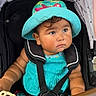 arms, baby, baby_clothes, bright_colors, child, curly_hair, cute, expression, face, hat, infant, outdoor, pink_shorts, portrait, seatbelt, sitting, stroller, summer_clothing, toy, turquoise