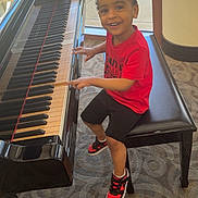 Ladedrick joined the competition — help win amazing prizes! child, piano, bench, indoor, carpet, window, smiling, red_shirt, black_shorts, sneakers, musical_instrument, happy, person, fingers, seated, young_boy, light, reflection, floor, casual_clothing