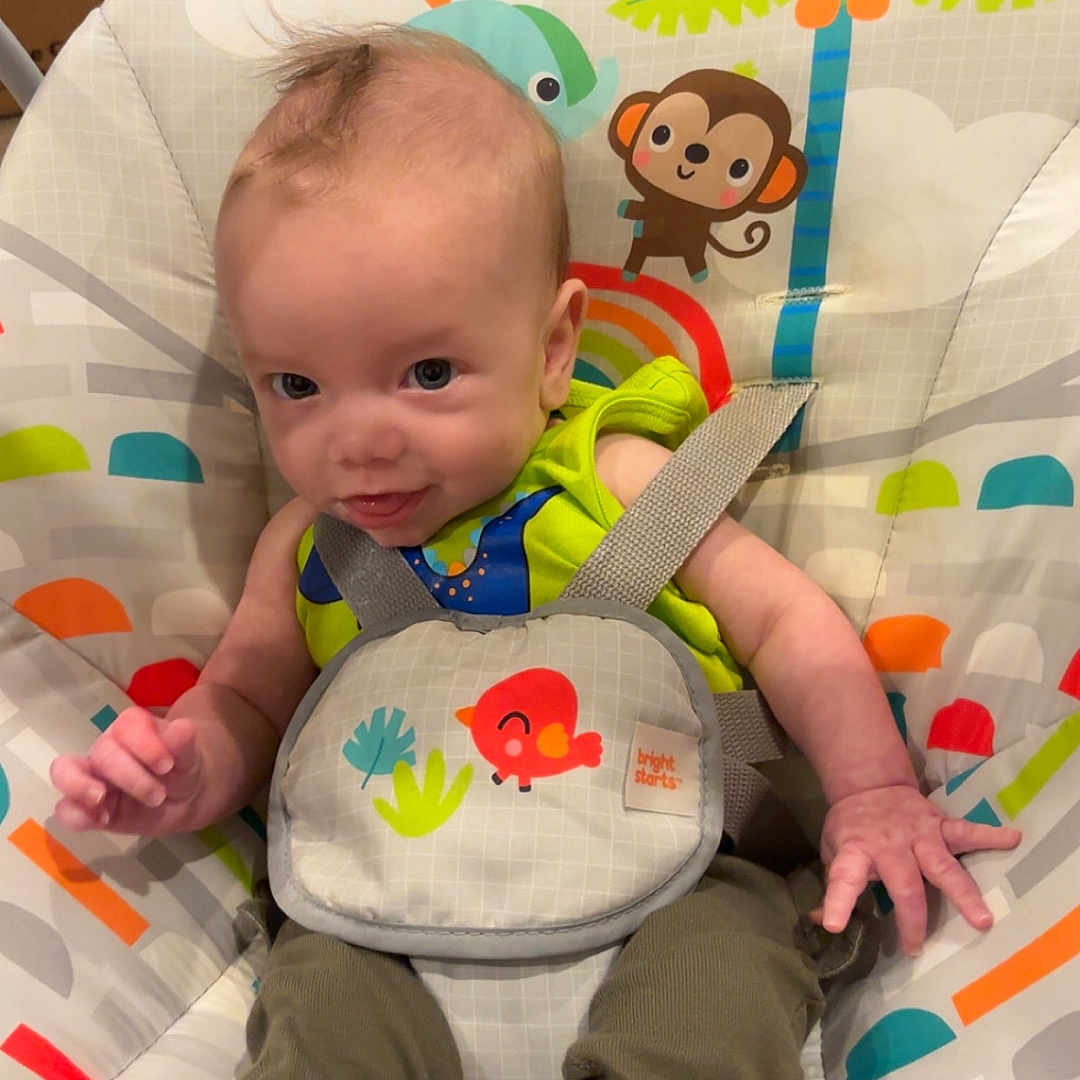 Hayden joined the competition — help win amazing prizes! baby, child, infant, baby_seat, colorful, animal_prints, monkey, toucan, rainbow, green_clothing, socks, happy, indoors, floor, cardboard_box, water_bottles, smile, cute, playful, straps