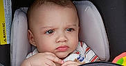 Luis joined the competition — help win amazing prizes! baby, blanket, child, closeup, clothing, cushion, eyes, fabric, face, hair, hands, indoors, infant, portrait, seated, serious, striped_shirt, stroller, toy, transportation