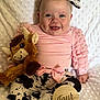 baby, infant, smile, pink_clothing, ruffled_sleeves, cow_print, headband, bow, plush_toy, triceratops, wooden_sign, four_months, milestone, sitting, white_blanket, happy, cute, portrait, child, indoors