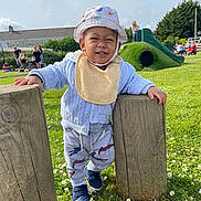 Markley Amari is registered to the contest to win money with this photo: bib, child, cute, daisies, daylight, fun, grass, hat, nature, outdoor, pants, park, people, playground, shoes, slide, smiling, sweater, toddler, wooden_posts