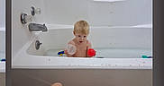 Keagan is registered to the contest to win money with this photo: bath_time, bathroom, bathtub, blond_hair, blue_toy, child, faucet, home, indoor, legs, phone_screenshot, portrait, reaction_icons, red_ball, sitting, tattoo, toddler, toy, water, white_tub