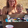 baby, woman, birthday_cake, cardboard_box, outdoor, picnic_table, red_cup, celebration, sunlight, happy, child, face, smile, table, food, party, grass, summer, people, event