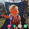 toddler, child, blue_chair, outdoor, night, patriotic_clothing, american_flag, grass, stroller, fence, adult, person, phone_screen, app_icons, search_bar, volume_control, face, light, sitting, casual