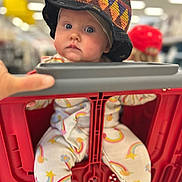 Tulsi joined the competition — help win amazing prizes! baby, infant, child, hat, shopping_cart, store, aisle, portrait, blue_eyes, chubby_cheeks, onesie, rainbow_pattern, bokeh, shallow_depth_of_field, seat, hand, red_plastic, cute, looking_at_camera, portrait_mode