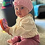 baby, infant, child, pink_hat, knitted_hat, bow, blue_eyes, cheeks, white_blouse, pink_pants, toy, round_toy, sitting, carpet, indoor, portrait, close_up, bokeh_background, soft_lighting, cute