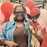 Gin Gin is registered to the contest to win money with this photo: woman, person, dog, puppy, pet, portrait, smiling, glasses, braids, denim_jacket, black_shirt, bandana, red, balloons, party, indoor, holding_pet, sitting, celebration, photography