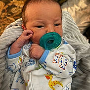 Beau is registered to the contest to win money with this photo: baby, infant, pacifier, onesie, animal_print, blanket, sleepwear, child, newborn, cute, soft, cozy, hand, face, portrait, indoors, resting, young, person, clothing