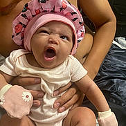 Nalani joined the competition — help win amazing prizes! baby, infant, mittens, bonnet, pink, hand, person, skin, expression, yawn, cute, newborn, clothing, holding, portrait, indoor, adult, bare_torso, sleepy, closeup