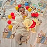 Aris is registered to the contest to win money with this photo: baby, blanket, bunny_pattern, plush_toy, pooh_bear, red_balls, yellow_balls, storybooks, child, indoor, soft_toys, cute, cozy, infant, clothing, laying_down, playtime, colorful, nursery, comfort