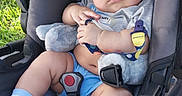 Aris is registered to the contest to win money with this photo: baby, stroller, blue_cap, plush_toy, blue_socks, shorts, outdoor, grass, child, cute, infant, seat_belt, car_seat, sunlight, person, portrait, baby_boy, casual_clothing, resting, expression