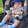 baby, stroller, blue_cap, plush_toy, blue_socks, shorts, outdoor, grass, child, cute, infant, seat_belt, car_seat, sunlight, person, portrait, baby_boy, casual_clothing, resting, expression