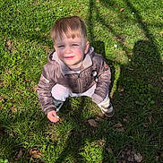 Zayn a rejoint le concours — aidez-le/la à gagner de superbes lots ! cheek, child, daisy, face, grass, hand, jacket, leaves, nature, outdoor, park, portrait, shadow, shoes, sitting, smiling, spring, squinting, sunlight, toddler