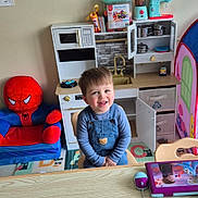 Zayn participe au concours pour gagner de l'argent avec cette photo : armchair, chair, child, computer_mouse, denim_overalls, faucet, floor_mat, happy, play_tent, playroom, portrait, pots_and_pans, sink, smiling, stuffed_spiderman, tablet_device, toddler, toy_blender, toy_kitchen, wooden_table