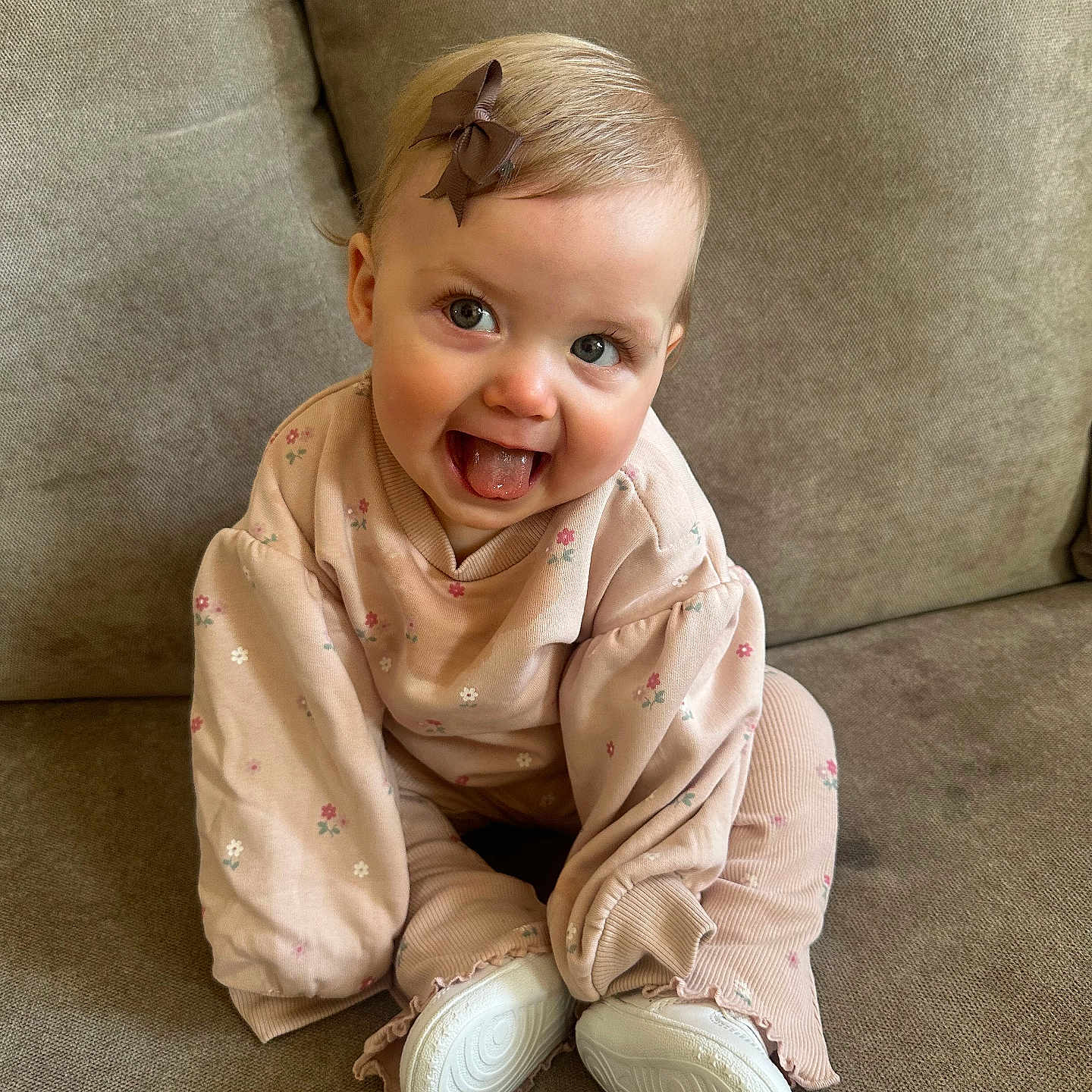 Remi-Rose joined the competition — help win amazing prizes! baby, bow, casual_clothing, child, couch, cozy, cute, face, floral_pattern, happy, indoor, infant, person, pink_clothing, playful, sitting, smiling, sofa, tongue_out, white_shoes
