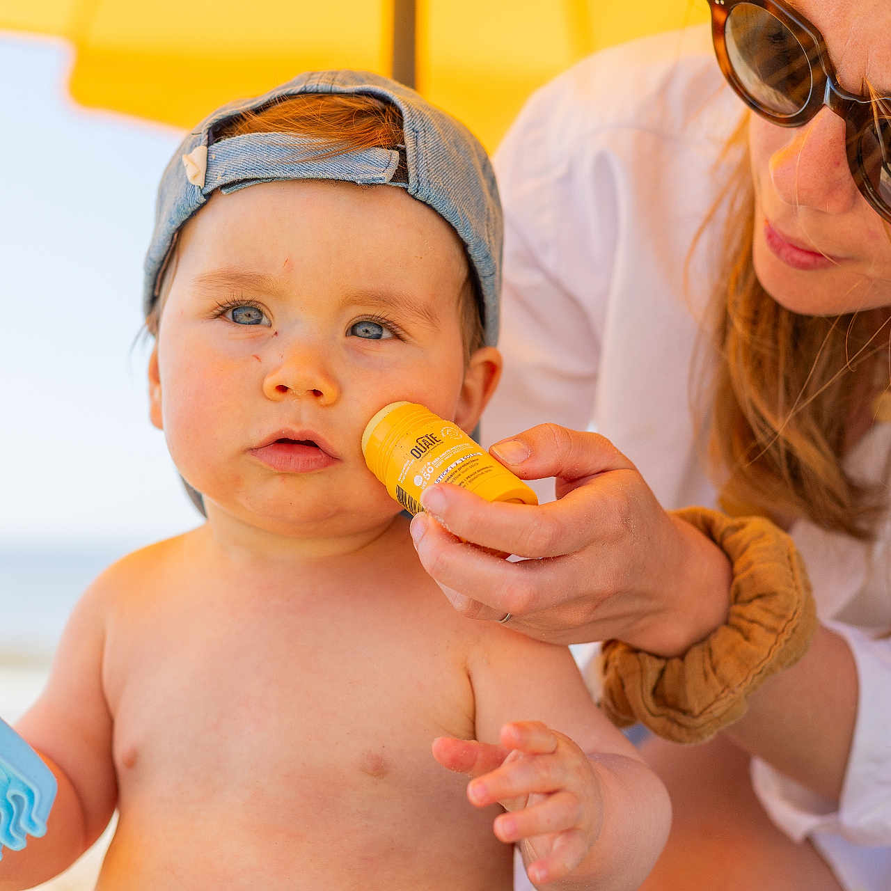 Edgard a rejoint le concours — aidez-le/la à gagner de superbes lots ! adult, bare_chest, beach, blue_eyes, care, casual, child, family, hat, outdoor, protective, skin_care, striped_shorts, summer, sunlight, sunscreen, toddler, toy, umbrella, vacation