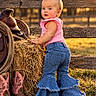 child, toddler, cowgirl, outdoor, portrait, smiling, blonde_hair, hair_bow, pink_shirt, denim, jeans, bell_bottoms, cowboy_boots, saddle, hay_bale, fence, farm, ranch, sunset, grass