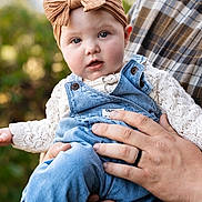 Ella is registered to the contest to win money with this photo: baby, child, infant, headband, bow, denim_overalls, knit_sweater, hand, plaid_shirt, outdoor, portrait, closeup, cute, curious, skin, face, person, holding, soft_light, nature