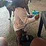 toddler, child, indoor, carpet, sippy_cup, diaper, pink_clothing, black_sandal, nike, dog, blue_collar, table, furniture, household, floor, person, barefoot, living_room, pet, casual