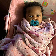 Harmony is registered to the contest to win money with this photo: baby, blanket, pacifier, pink, child, infant, face, curly_hair, chair, pattern, soft_texture, indoor, cute, wrapped, portrait, looking, comfort, baby_clothes, seat, young