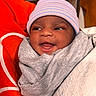Dream is registered to the contest to win money with this photo: newborn, baby, infant, child, face, smiling, happy, beanie, hat, blanket, swaddled, bundled, gray_clothing, red_background, portrait, close_up, indoors, cozy, eyes, mouth