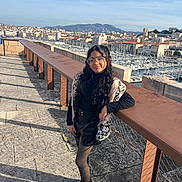 Ana Bheatriz participe au concours pour gagner de l'argent avec cette photo : child, girl, glasses, long_hair, black_clothing, faux_fur, handbag, boots, outdoor, cityscape, marina, boats, stone_pavement, railing, sunlight, shadow, mountains, sky, portrait, fashion