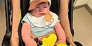 Joseph Vinícius participe au concours pour gagner de l'argent avec cette photo : baby, infant, stroller, hat, bib, plush_toy, yellow_toy, indoor, floor_tiles, socks, cute, child, seat_belt, toy, person, headwear, clothing, legs, hands, expression