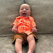 Jaxon joined the competition — help win amazing prizes! baby, child, smiling, happy, orange_shirt, brown_shorts, sitting, couch, indoor, infant, legs, feet, face, joyful, casual_clothing, human, cute, portrait, young_child, relaxed