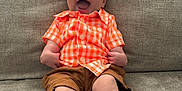 Jaxon joined the competition — help win amazing prizes! baby, child, smiling, happy, orange_shirt, brown_shorts, sitting, couch, indoor, infant, legs, feet, face, joyful, casual_clothing, human, cute, portrait, young_child, relaxed