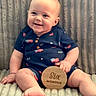 baby, infant, smiling, sitting, onesie, american_flag, wooden_sign, six_months, blanket, texture, cute, child, person, happy, portrait, indoor, soft_lighting, skin, feet, hand